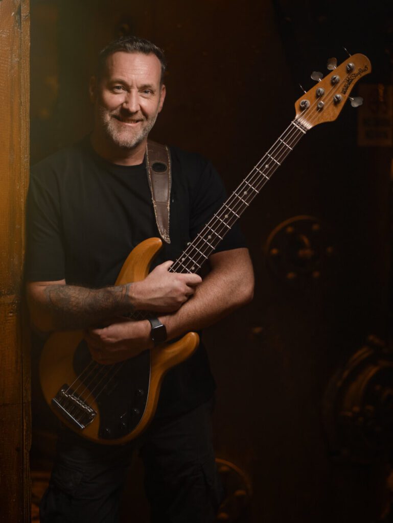 Jay Clarke is smiling and holding an electric bass guitar.