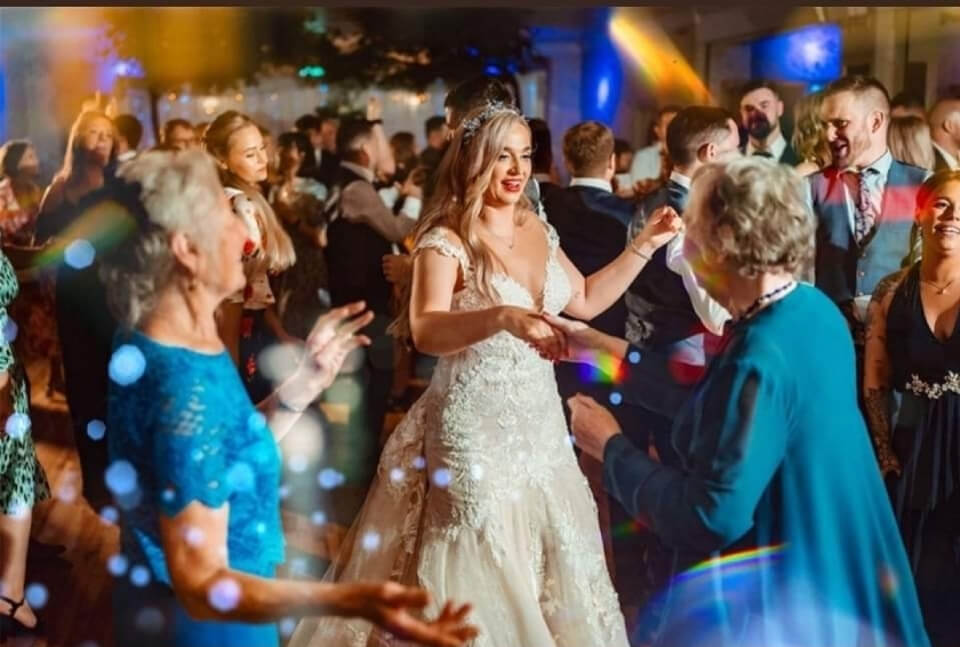 A bride dancing joyfully with guests at a lively wedding reception.